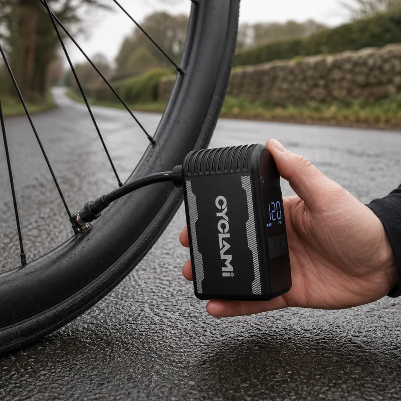 Black electric pump connected to a bicycle tyre on wet pavement